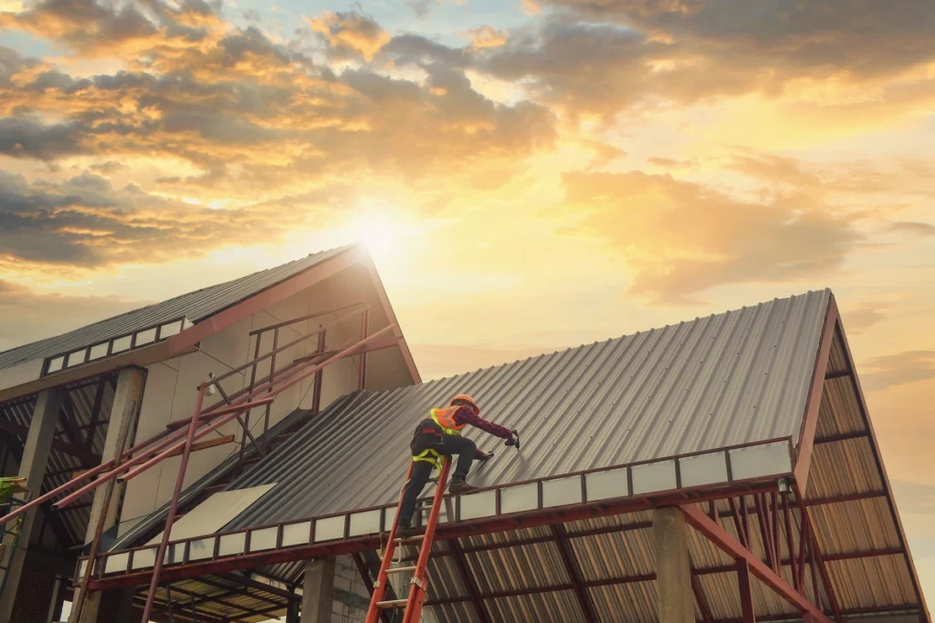 commercial roofing waunakee Sunset on commercial building worker installing metal roof