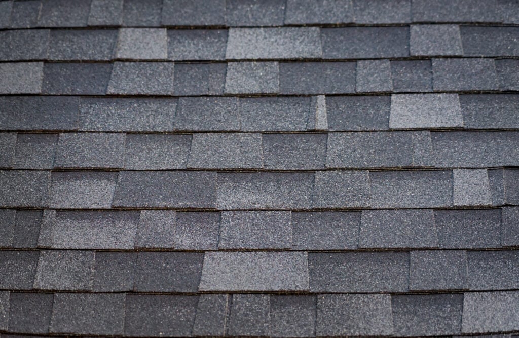 Close-up view of gray architectural shingles arranged in a uniform overlapping pattern, showcasing the textured and slightly varied surface of the roofing material.