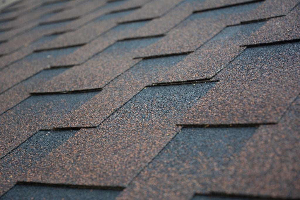 Close-up view of overlapping architectural shingles in shades of brown and black, arranged diagonally in a repeating pattern. architectural shingles