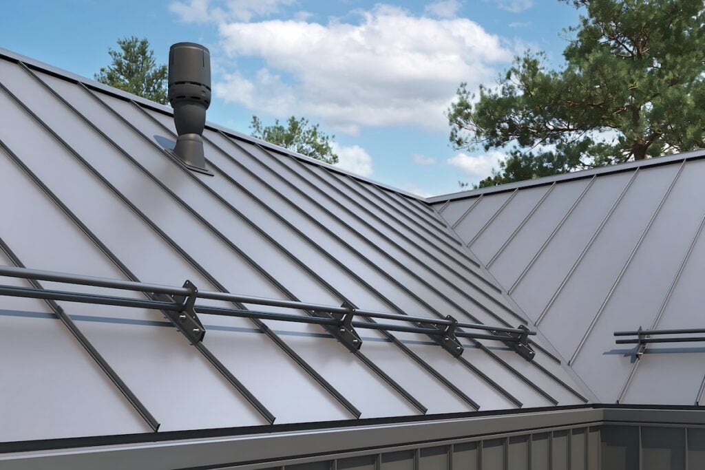 A standing seam metal roof with raised seams and snow guards lines the edge, nestled among pine trees beneath a partly cloudy sky. standing seam metal roof