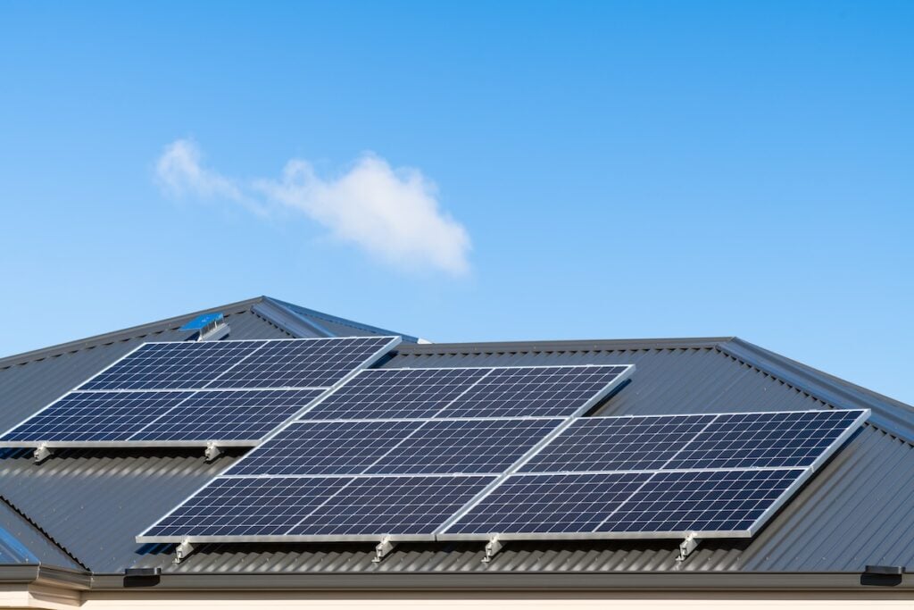 Several solar panels are installed on the roof of a building under a bright blue sky with a few clouds, positioned to capture sunlight efficiently and answer questions like how much energy does a solar panel produce. how much energy does a solar panel produce
