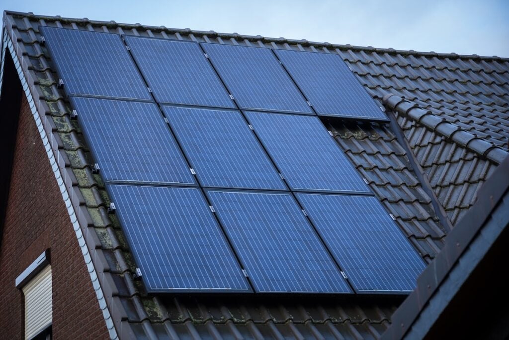 A close-up view of multiple solar panels with solar battery storage installed on the sloped, tiled roof of a house under a partly cloudy sky. solar battery storage