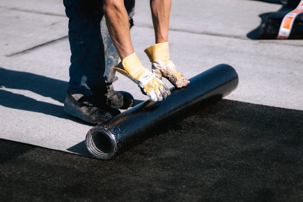 roofing membrane. Professional workers waterproofing house construction site. Worker rolling membrane