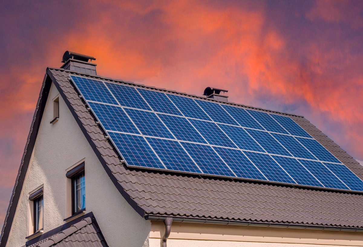 A house with solar panels installed on its sloped roof is shown at sunset, highlighting how many solar panels to power a house against an orange and purple sky in the background.