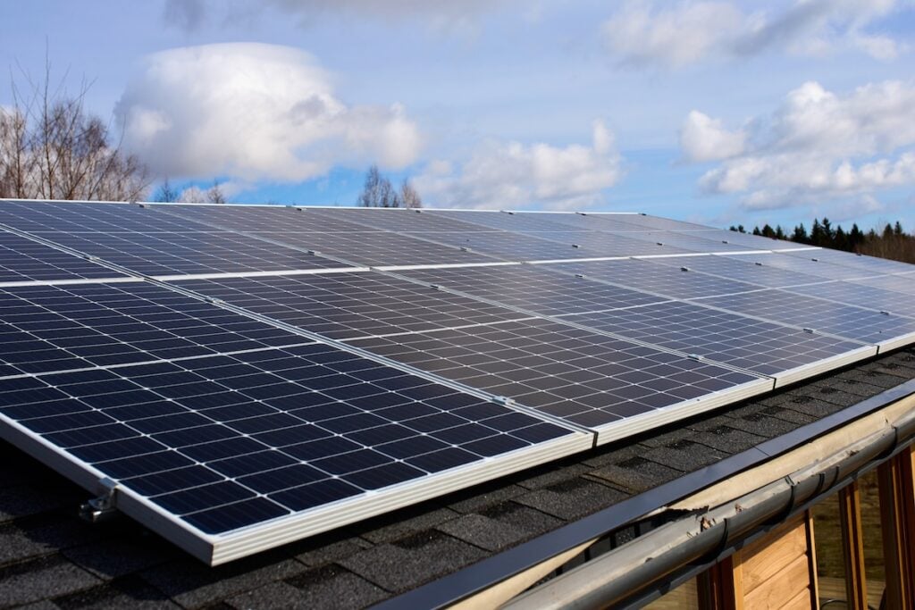 Rows of solar panels installed on the roof of a building, with a partly cloudy sky and some trees in the background—perfect inspiration for coming up with questions to ask solar companies about your own installation. questions to ask solar companies