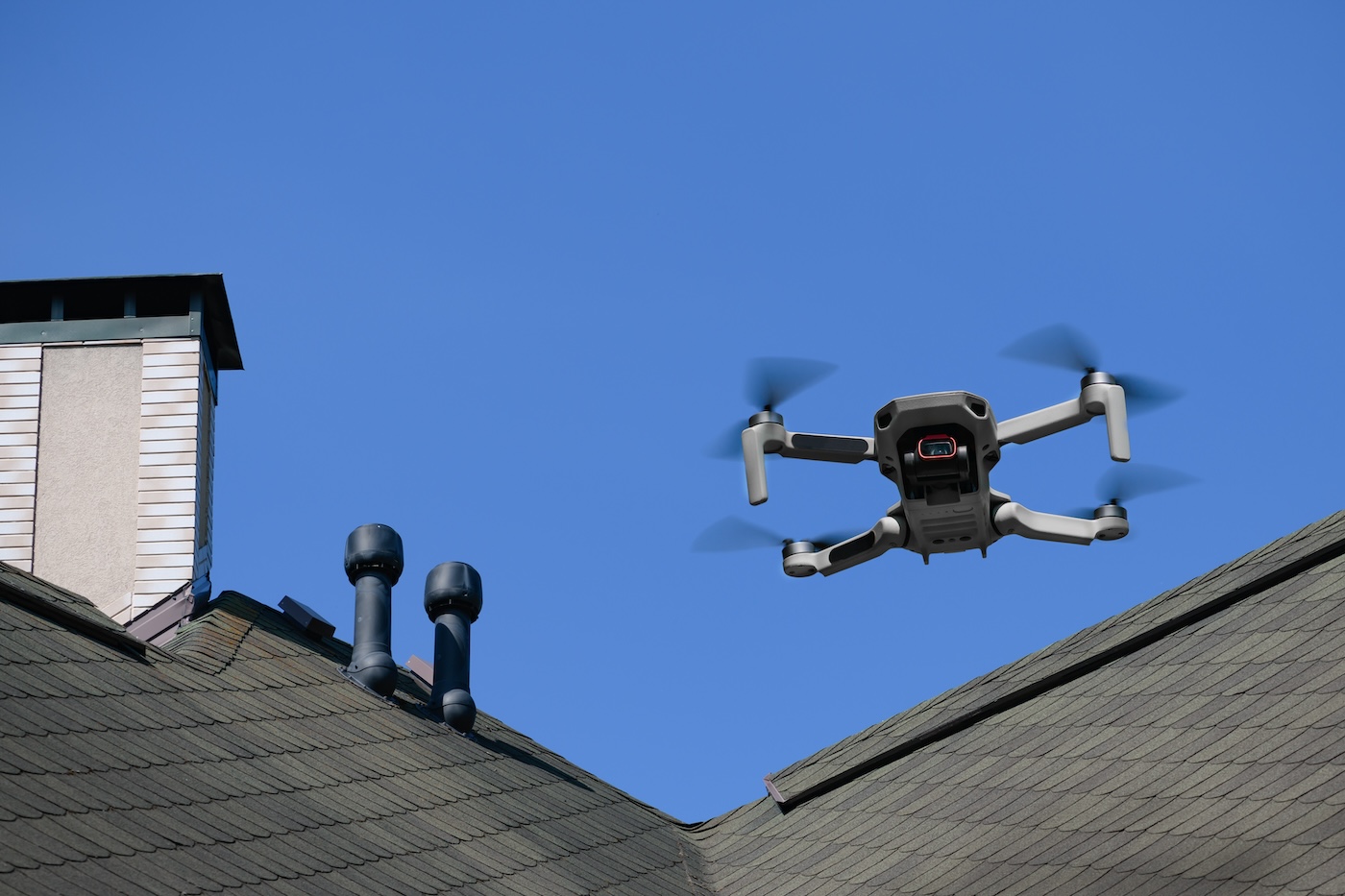 Drone in the air inspecting the roof over the house closeup on blue sky