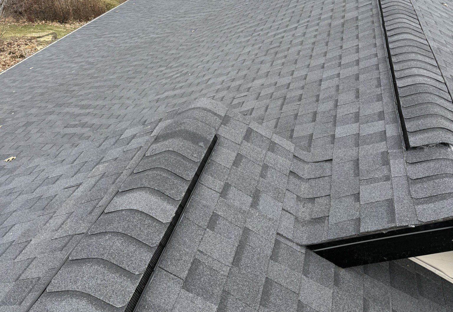 Close-up view of a dark gray asphalt shingle roof with intersecting ridges and valleys, showing the detailed pattern and texture of the roofing material.