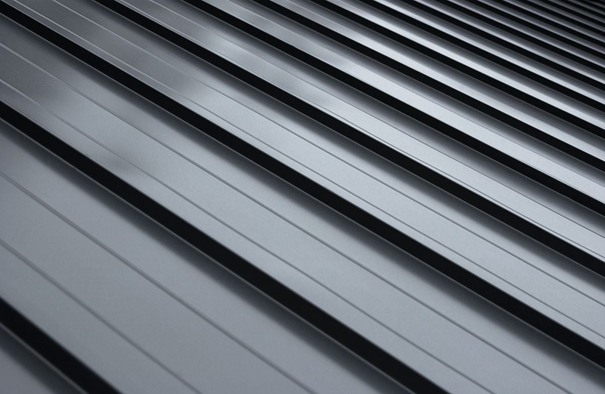 Close-up view of a modern metal roof with evenly spaced, parallel ridges and grooves, creating a sleek, geometric pattern in a silvery-gray color.