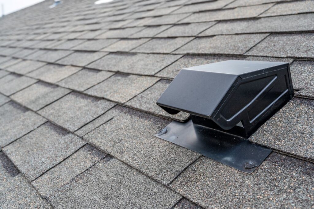 Close-up view of a residential roof with asphalt shingles, featuring a black metal roof vent installed among the shingles.