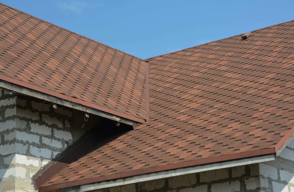 Brown asphalt shingled roof valley leaking problem area with a ventilation cap. A close-up of asphalt shingles installed on a roof valley with a waterproof flashing.