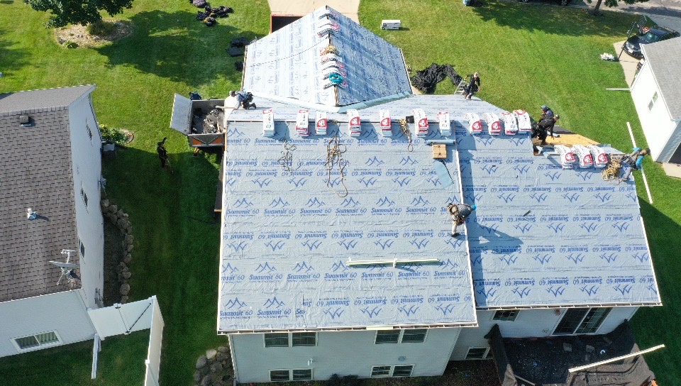 Aerial view of workers installing underlayment and roofing materials on a large residential house