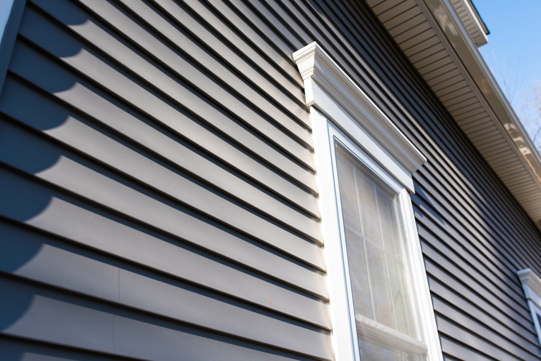 Close-up view of the exterior of a house with dark gray horizontal vinyl siding and a white-framed window under a gabled roof.