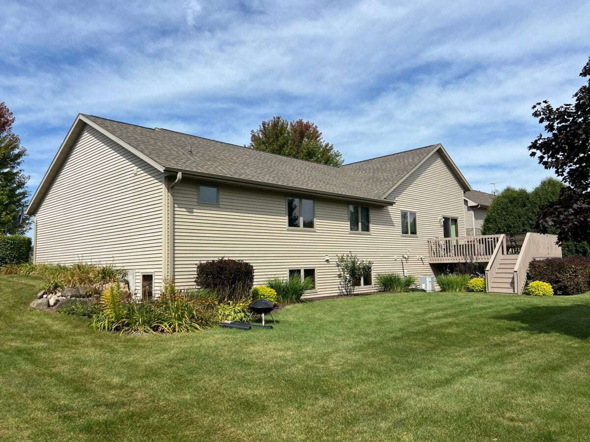 how much will it cost to fix a roof leak in waunakee wi A beige, single-story house with a fenced backyard, deck, and green lawn. There are shrubs, flowers, and a small black grill on the grass. The sky is partly cloudy.