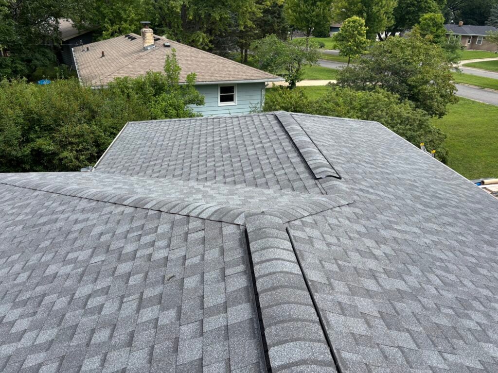 how much will it cost to fix a roof leak in waunakee wi A view from above of a gray shingled house roof with intersecting ridges; trees and neighboring houses are visible in the background.